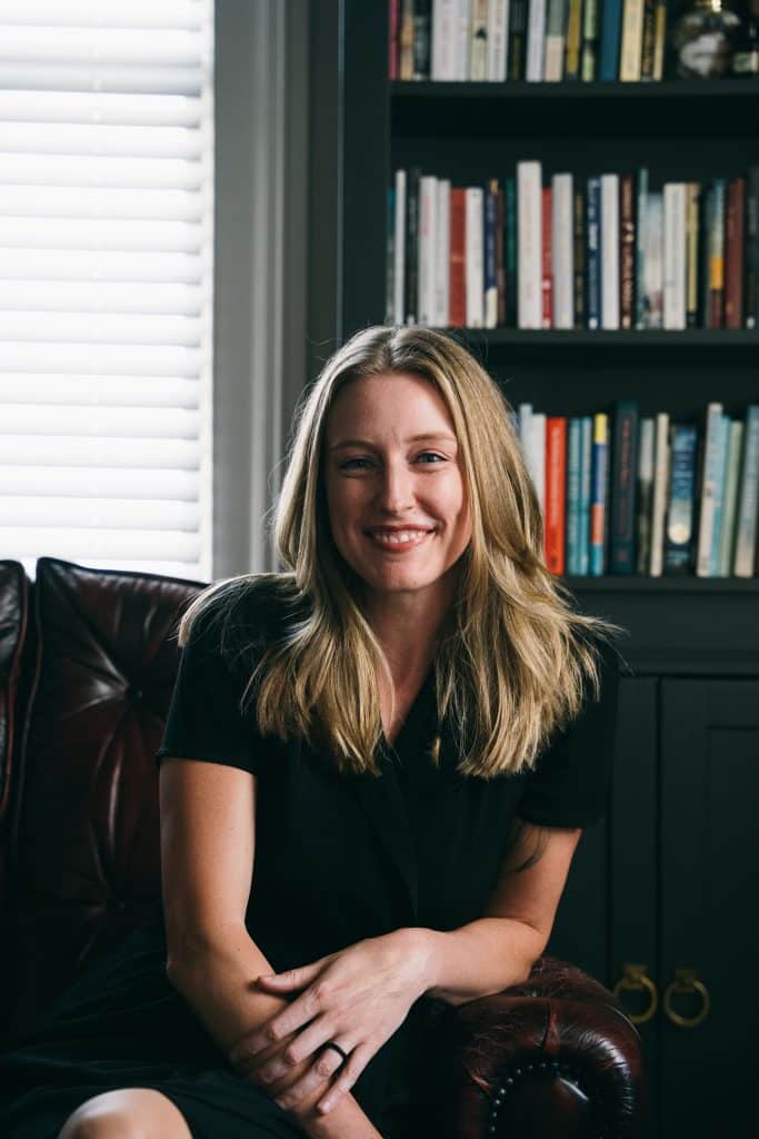 Smiling, blonde-haired woman sitting in front of a bookcase