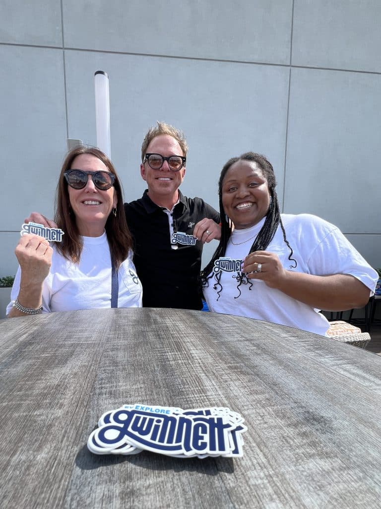 Two women and one man holding Explore Gwinnett stickers at an outdoor event