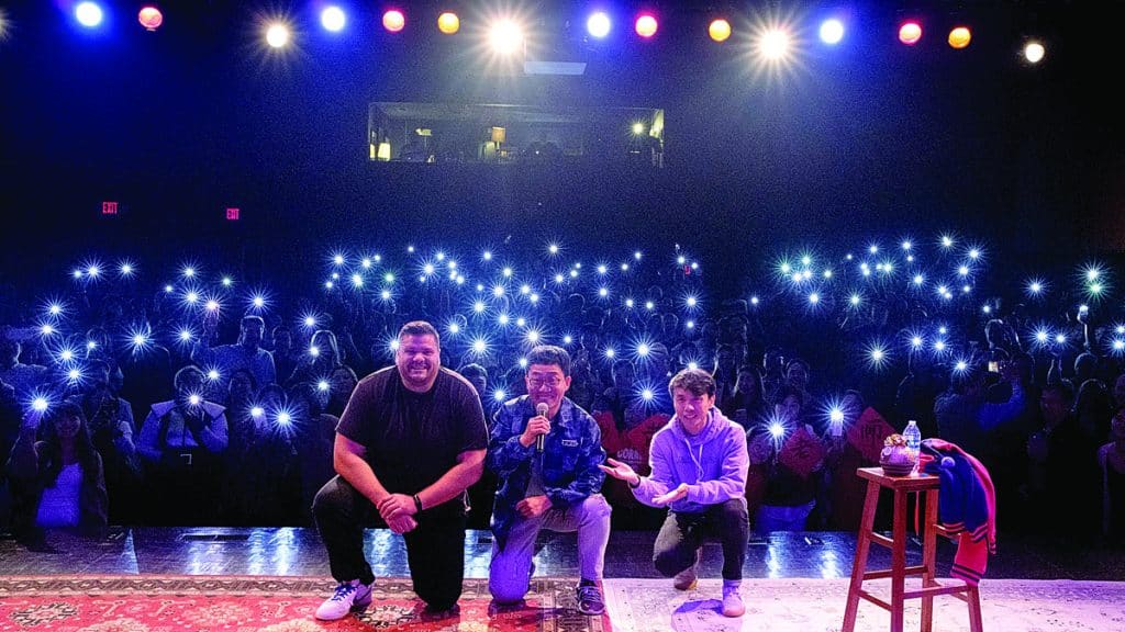 three guys on stage with an audience behind them