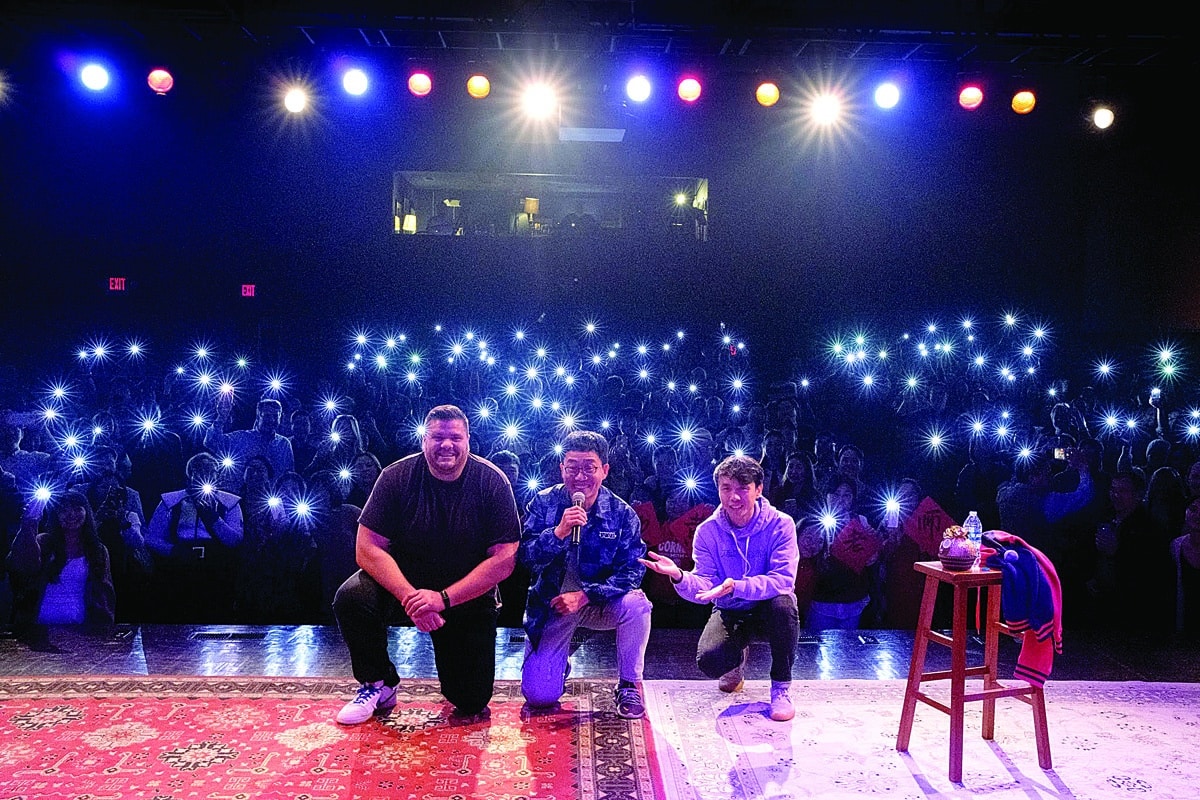 three guys on stage with an audience behind them