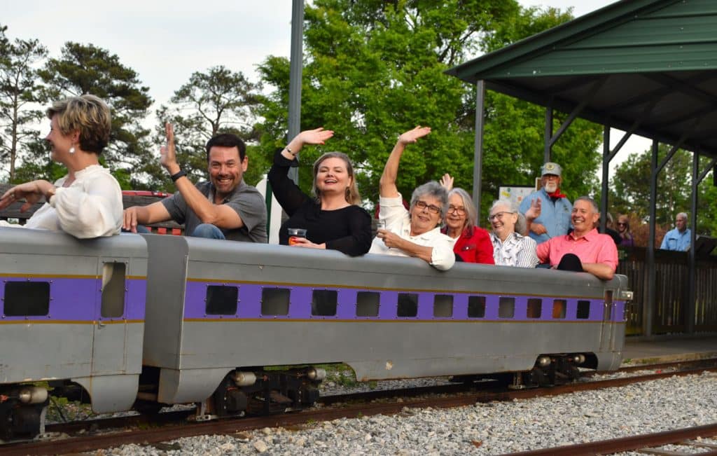 Adults riding on a small train at a private outdoor event