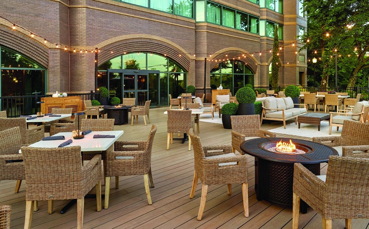 Outdoor dining space with tables, chairs and strings of lights at dusk