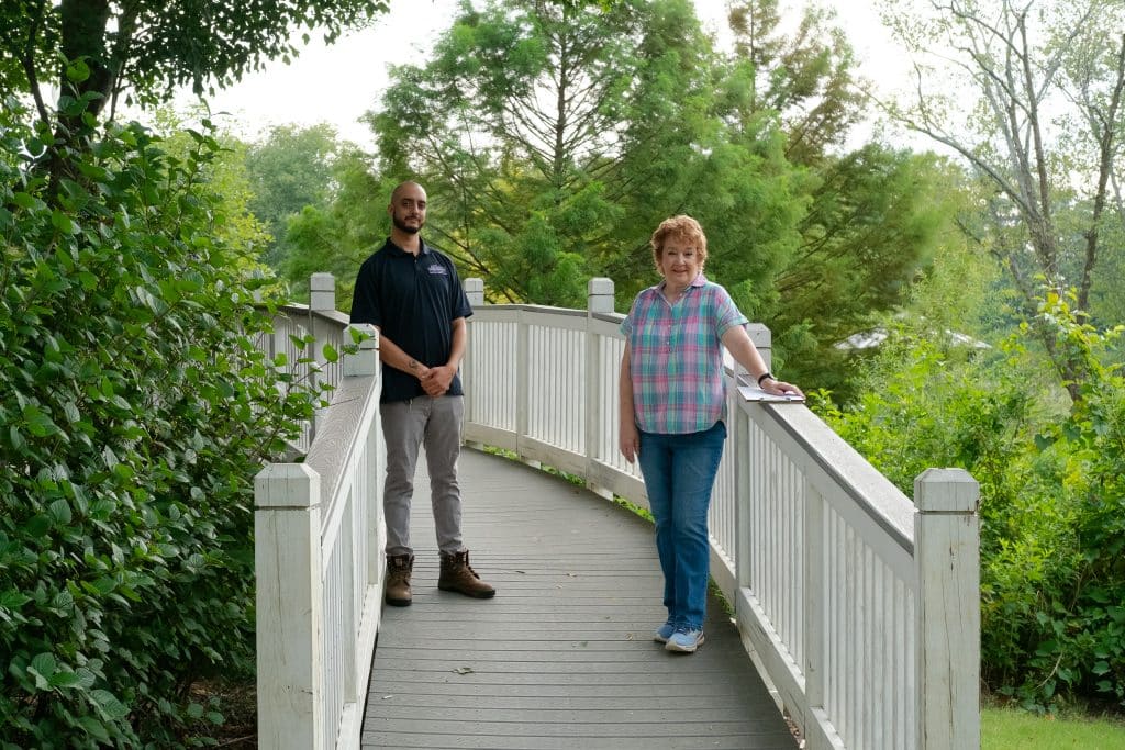 A man and a woman standing on a pedestrian bridge surrounded by trees