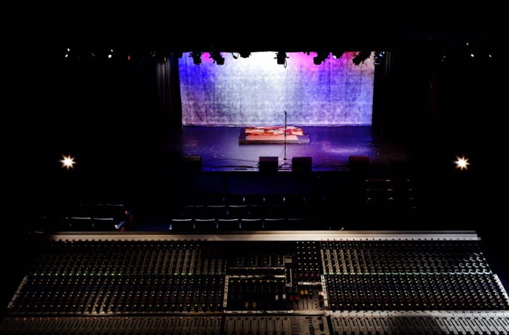 a stage with pink and purple lighting and a sound mixing board