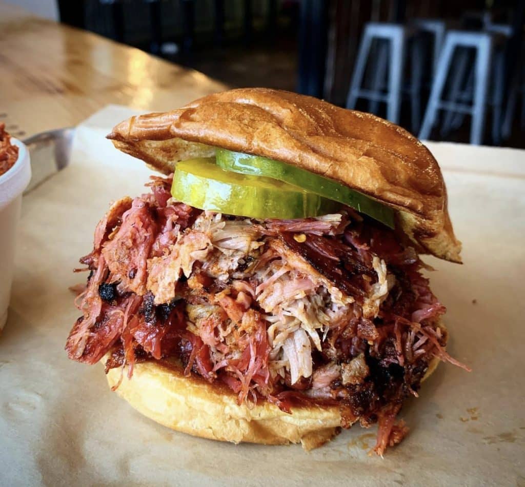 Pulled pork BBQ sandwich with pickles on a tray with brown paper