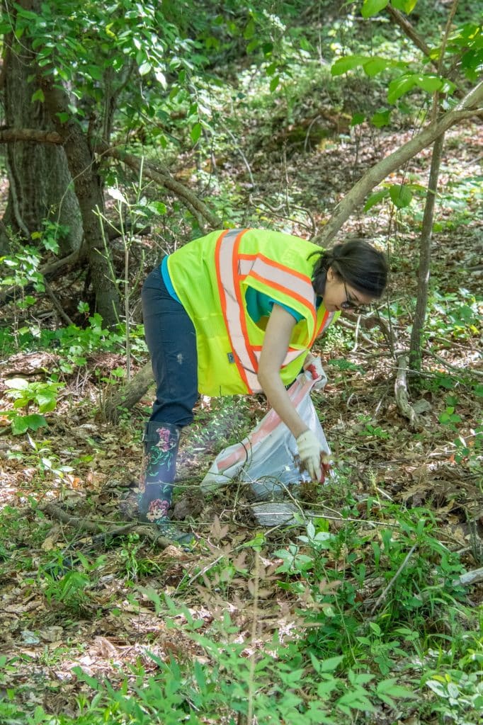 volunteer picking up trash in wooded area