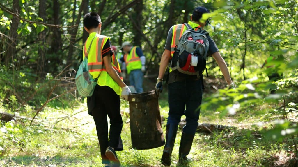 people carrying away trash cleaned up from a wooded area