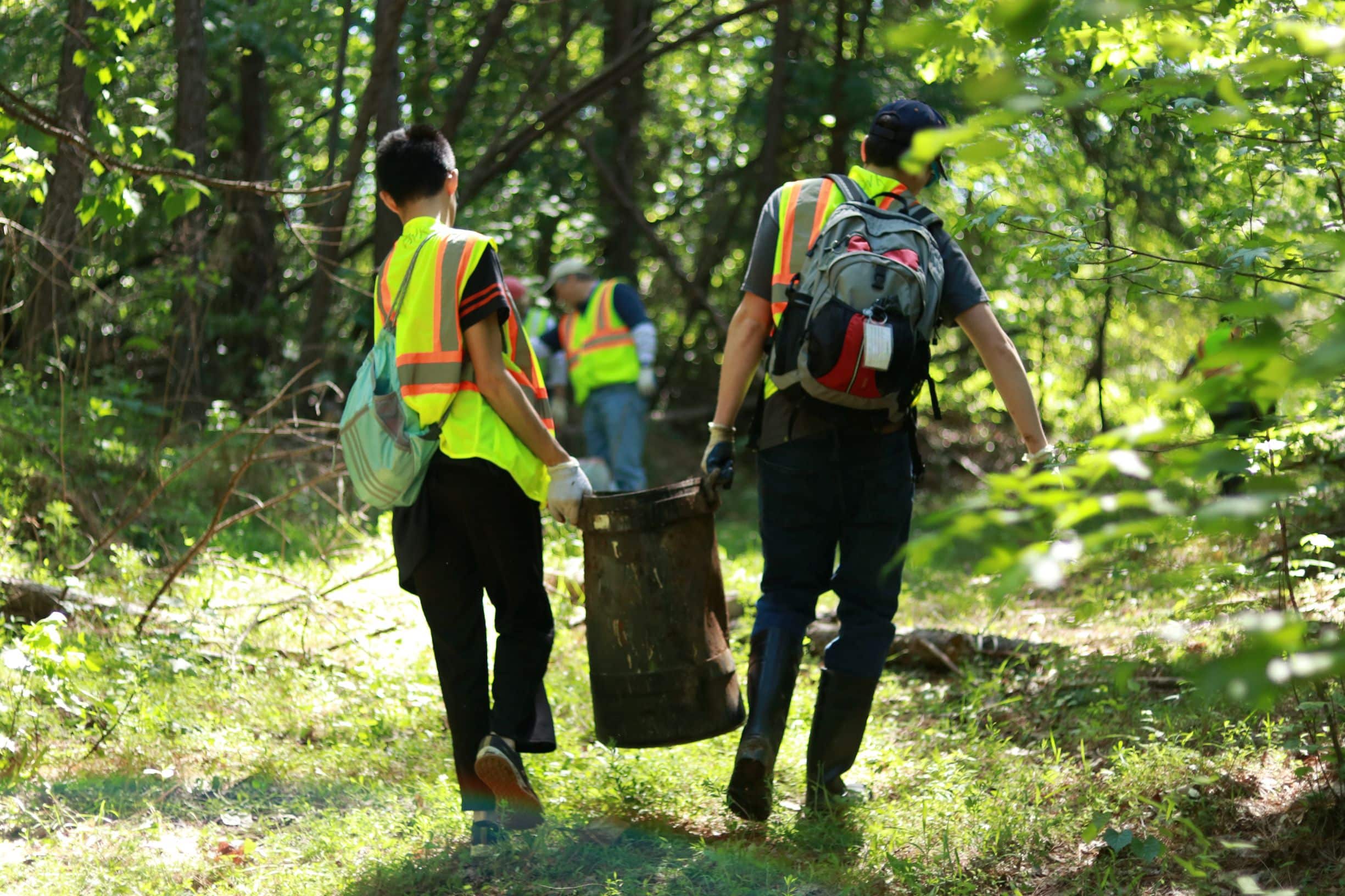 people carrying away trash cleaned up from a wooded area