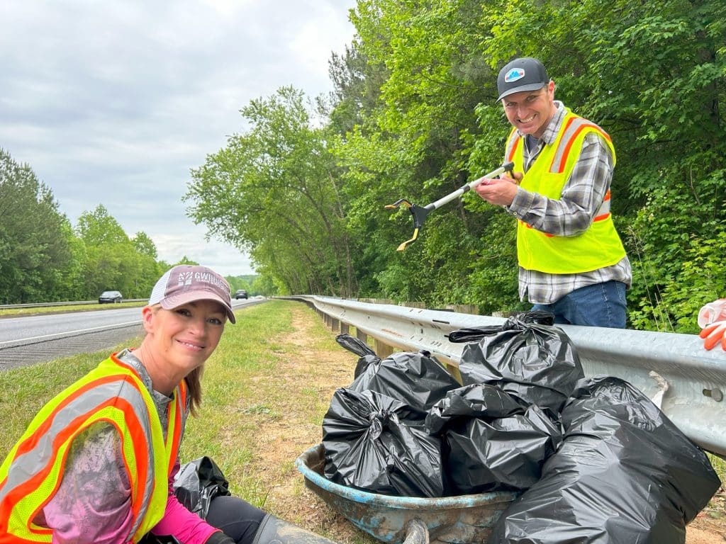 two volunteers picking up trash along the highway and a wooded area