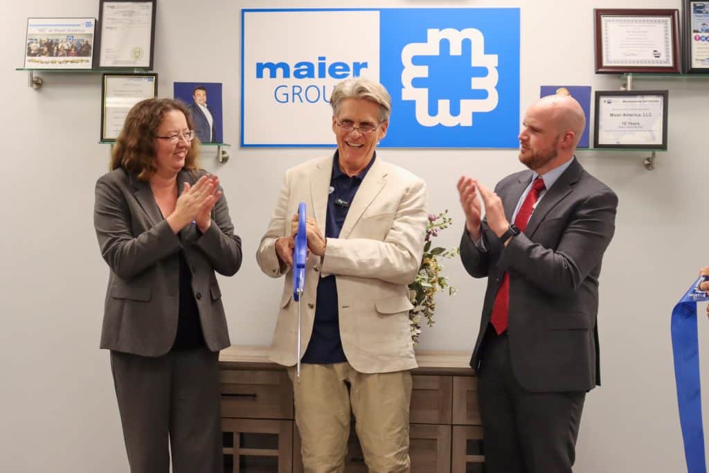 Three people standing in front of a sign indoors, clapping