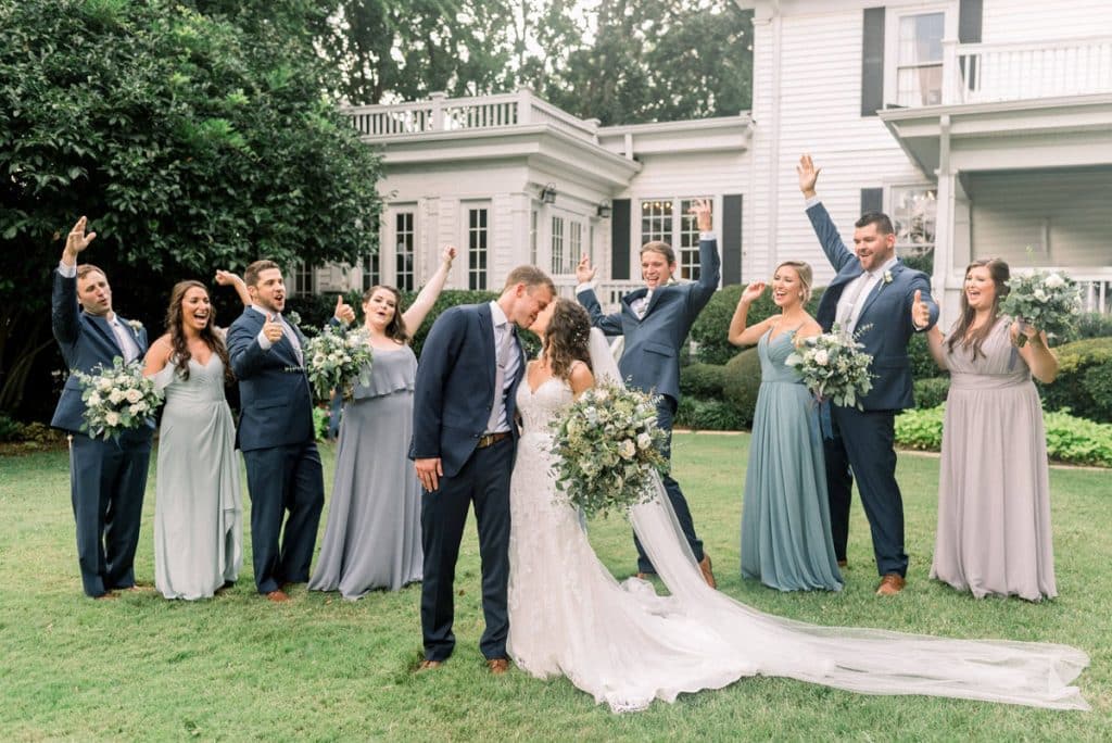 Bride and groom kissing outside in front of historic house with guests surrounding them