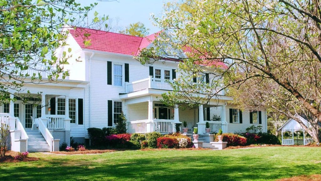 exterior view of historic white house with red roof and green grass and trees