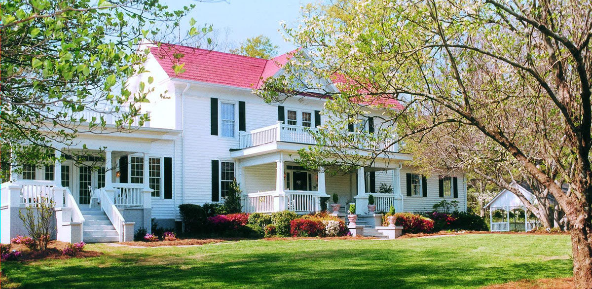 exterior view of historic white house with red roof and green grass and trees