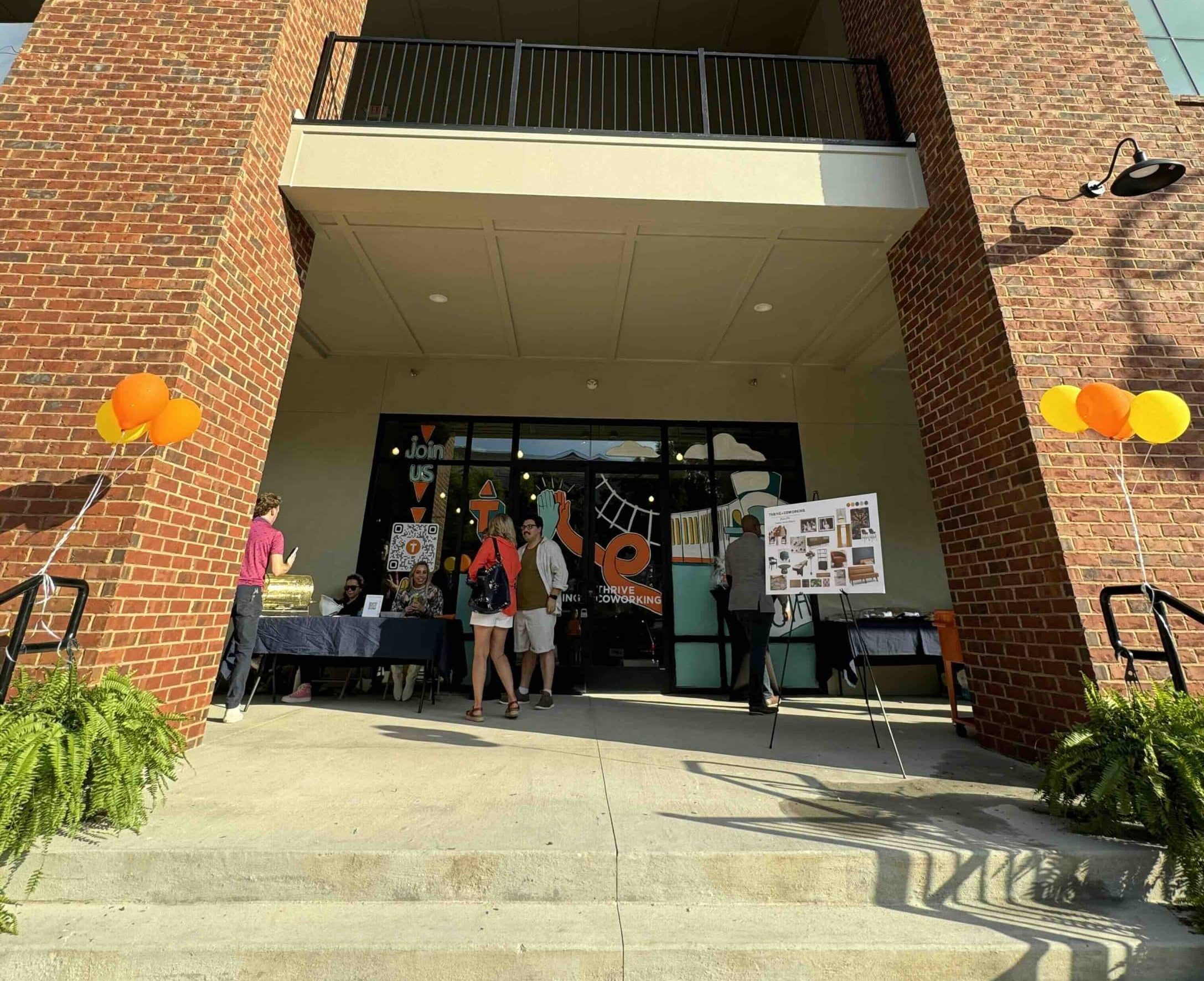 Exterior of two story office building with signs, balloons and few people in front for a grand opening party