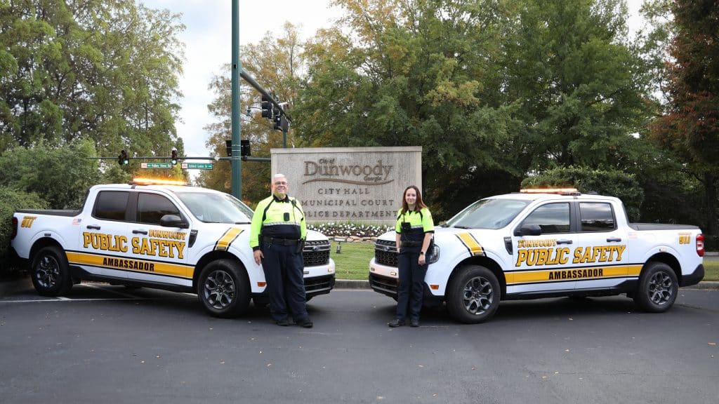 Two Dunwoody Police Public Safety Ambassadors standing next to official vehicles