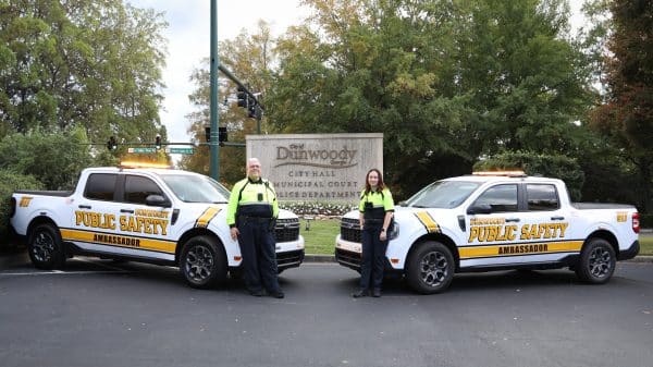 Two Dunwoody Police Public Safety Ambassadors standing next to official vehicles