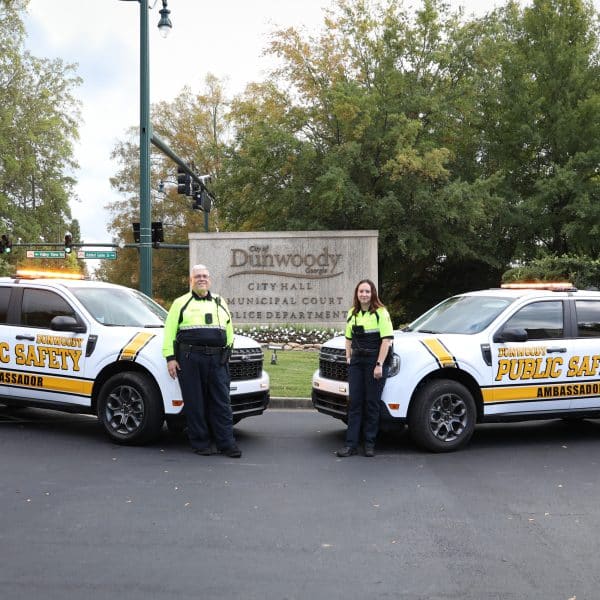 Two Dunwoody Police Public Safety Ambassadors standing next to official vehicles