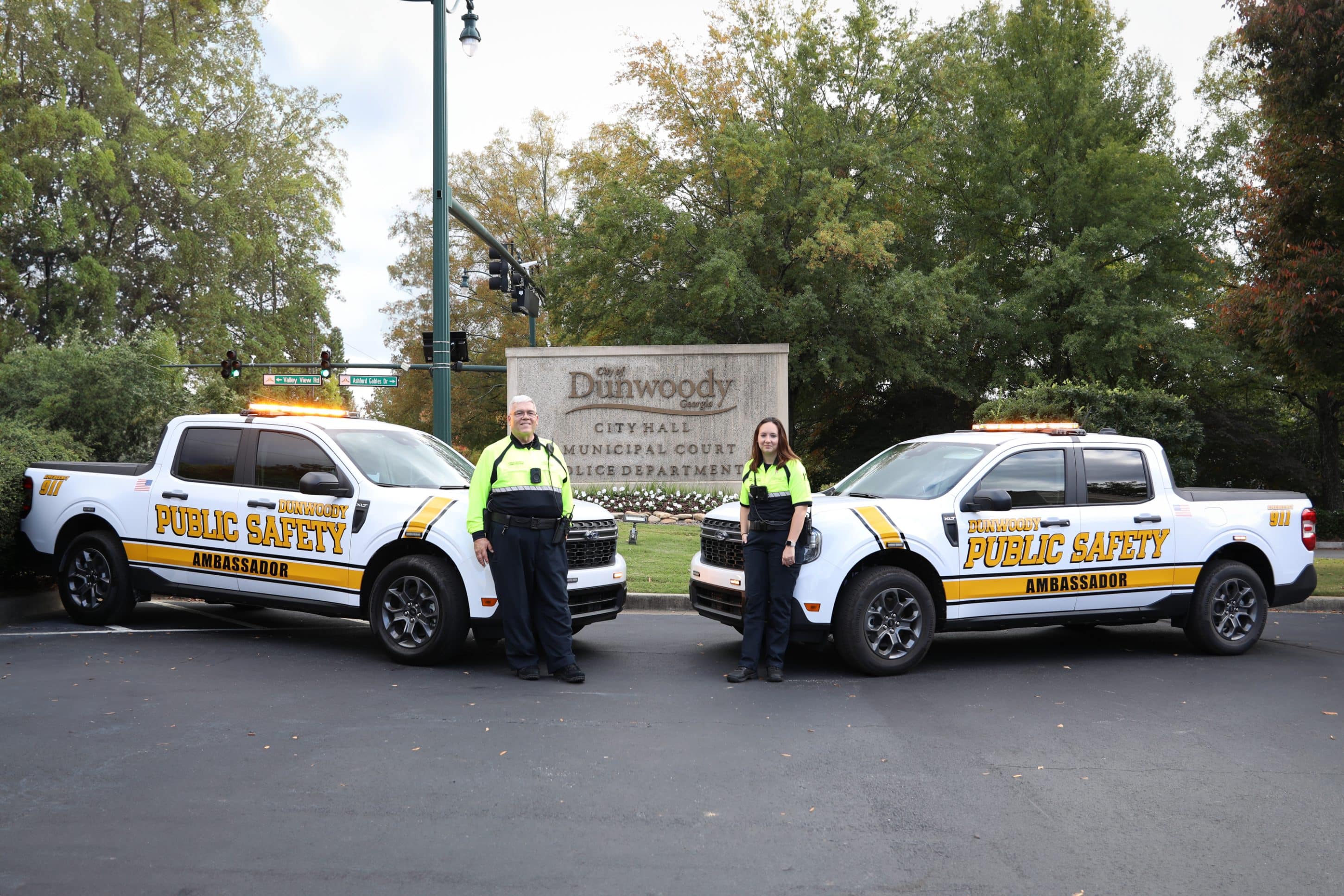 Two Dunwoody Police Public Safety Ambassadors standing next to official vehicles