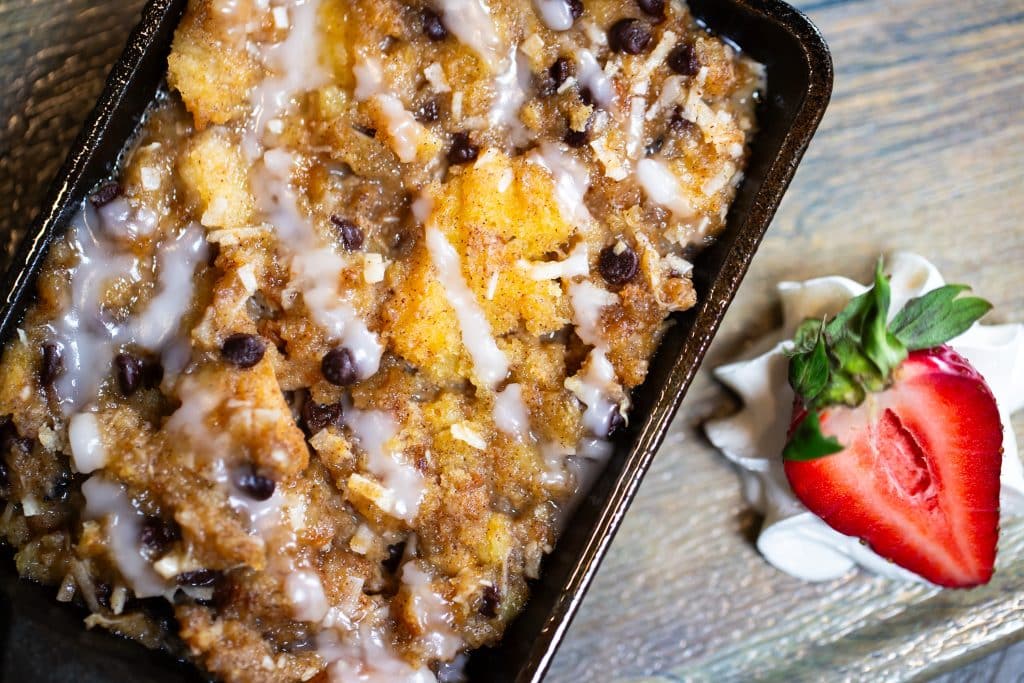 a pan of bread pudding on a table with a sliced strawberry next to it