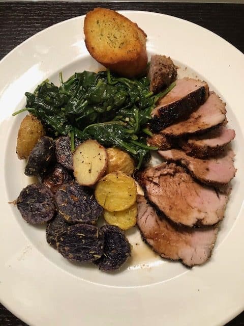 Sliced pork tenderloin with spinach and potatoes on a white plate