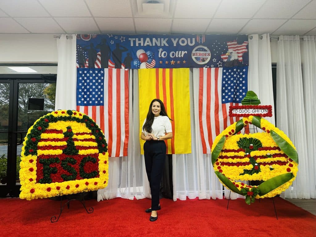 Woman standing on a red stage with flag banners behind her at a Veteran's Day celebration