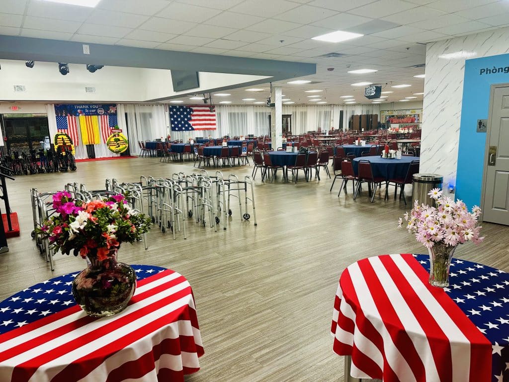 Large indoor gathering space with tables, chairs, donated walkers and other items, and American flag decorations for Veterans Day