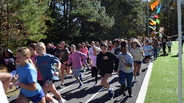 Group of middle school kids running on a track with green trees behind them