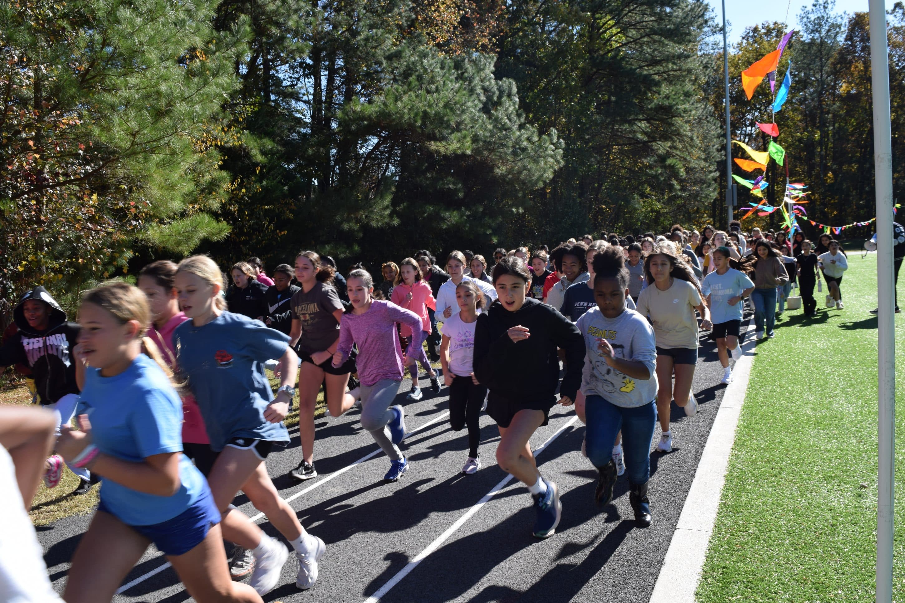 Group of middle school kids running on a track with green trees behind them