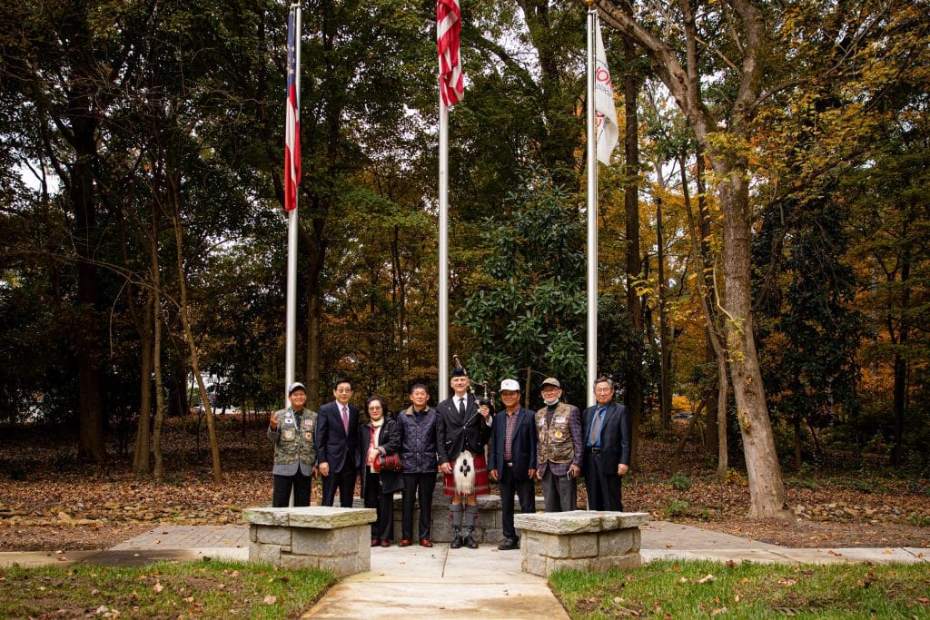 U.S. Military veterans standing at a Veterans' Memorial beneath three flags