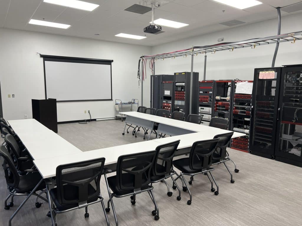 Very clean, well-lit conference room with a large u-shaped table and office chairs. The walls are white and equipment lines the right side of the room.