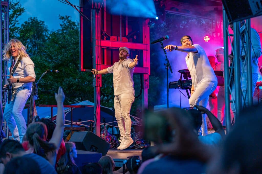 A band performing onstage at an outdoor July 4th concert as the sun goes down