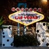 Replica of the famous Las Vegas sign alongside plants and giant dice at a Las Vegas-themed event.