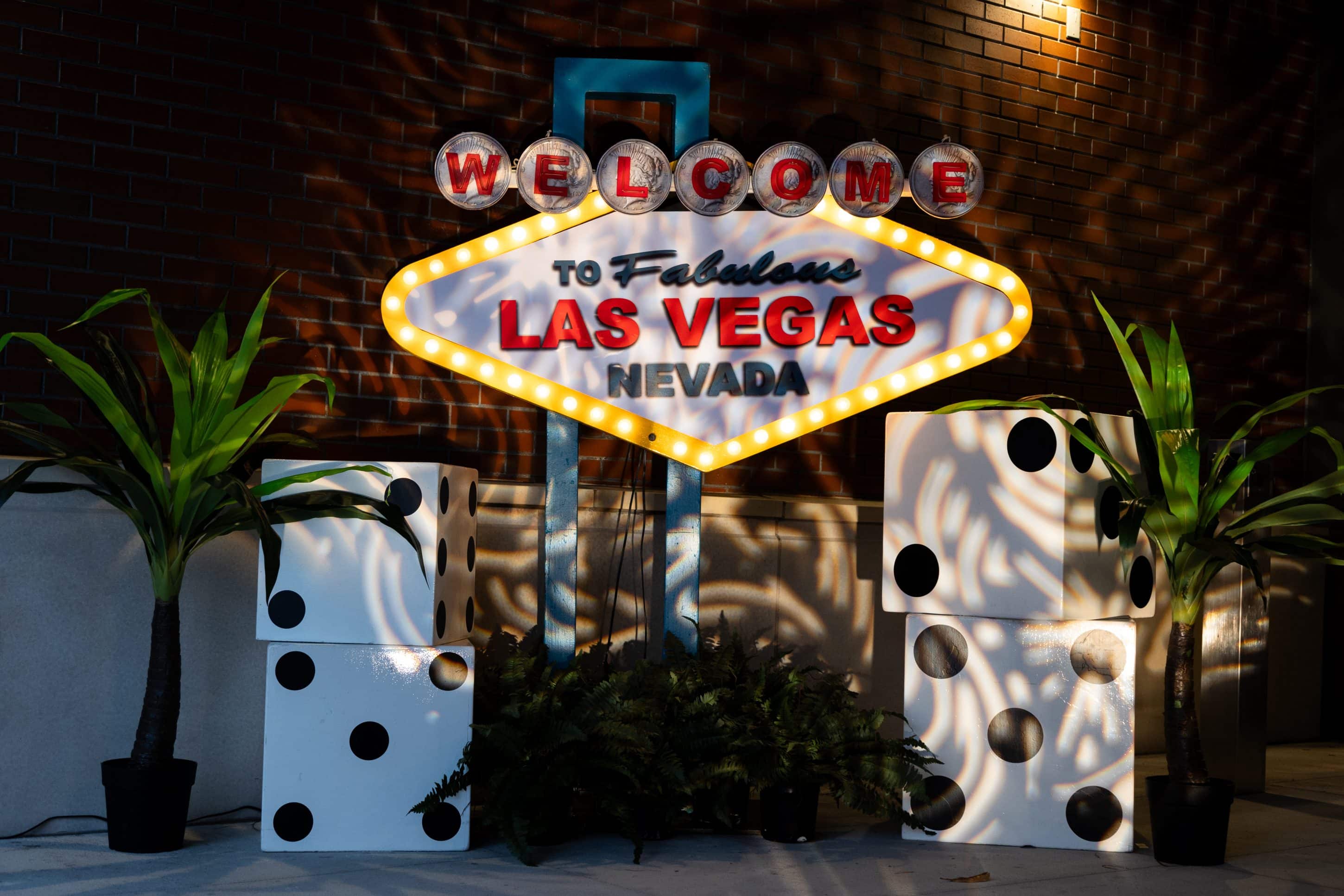 Replica of the famous Las Vegas sign alongside plants and giant dice at a Las Vegas-themed event.