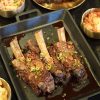 Korean BBQ ribs and side dishes served in separate plates on a black table. The ribs are covered with tiny sliced red peppers and green onions.