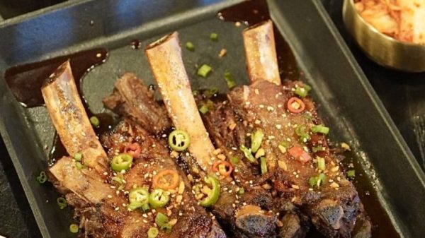 Korean BBQ ribs and side dishes served in separate plates on a black table. The ribs are covered with tiny sliced red peppers and green onions.