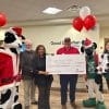 A group of people from Good Samaritan Gwinnett and Chick-fil-A standing in the waiting area of GSG, holding a giant check. There are red and white balloons, a Chick-fil-A cow mascot in a Santa suit. The check represents a $125,000 donation grant to GSG.