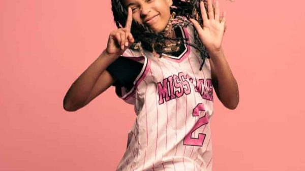 Black female teenager jumping into the air with a happy expression against a pink background.