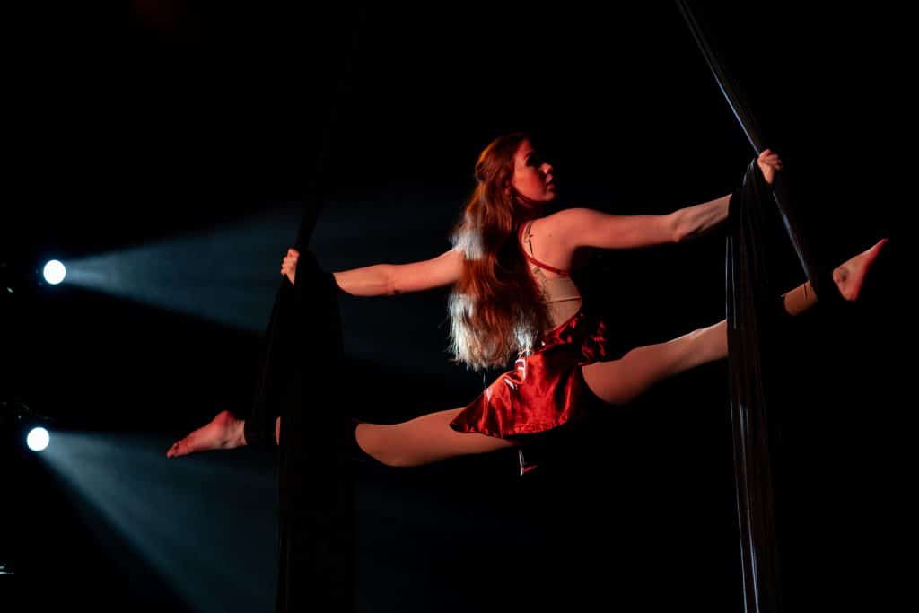 Female aerial acrobat doing a split in-air during a performance.