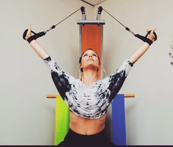 Woman with hair pulled back in ponytail, looking up towards the ceiling, using stretch bands at a small wellness center.