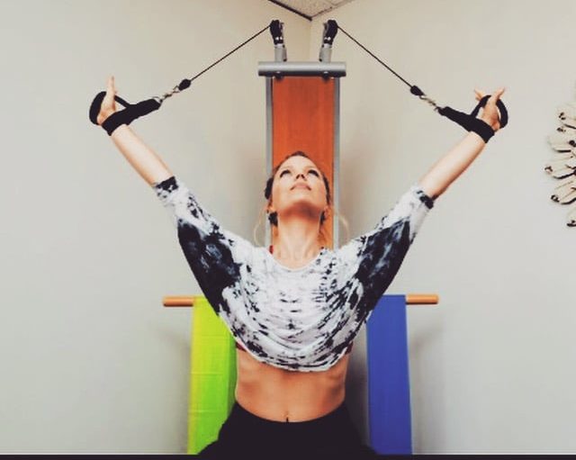 Woman with hair pulled back in ponytail, looking up towards the ceiling, using stretch bands at a small wellness center.