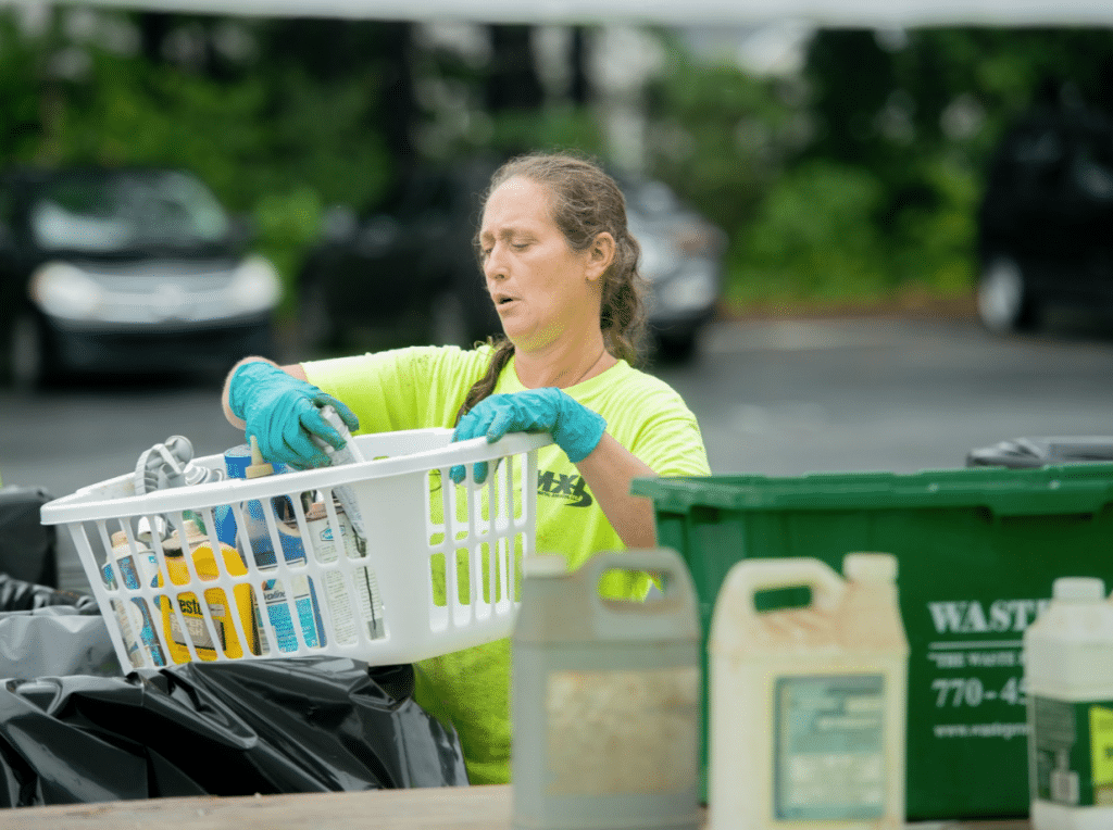 Woman wearing blue rubber gloves sorting hazardous household waste at a collection event.