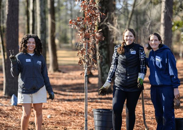 Three young women in a wooded area planting trees with City of Dunwoody on MLK Day of Service 2025.