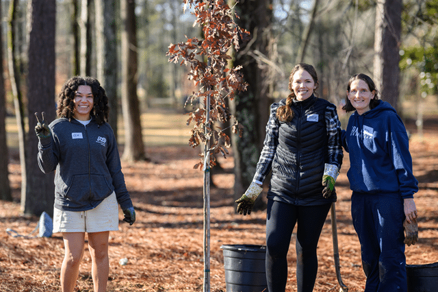 Three young women in a wooded area planting trees with City of Dunwoody on MLK Day of Service 2025.