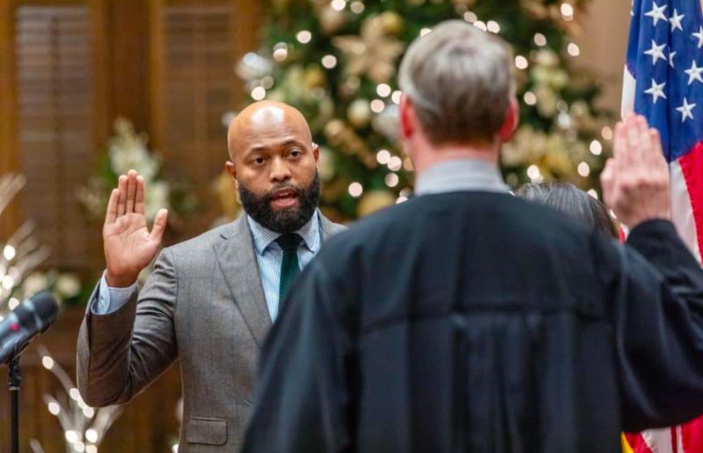 Kirkland Carden being sworn in by a judge as Commissioner of Gwinnett County District 1. There is an American flag on the right side of the photo and a Christmas tree with lights in the back ground.