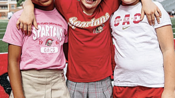 Three young girls wearing red, white and pink smiling for the camera at GAC summer camp