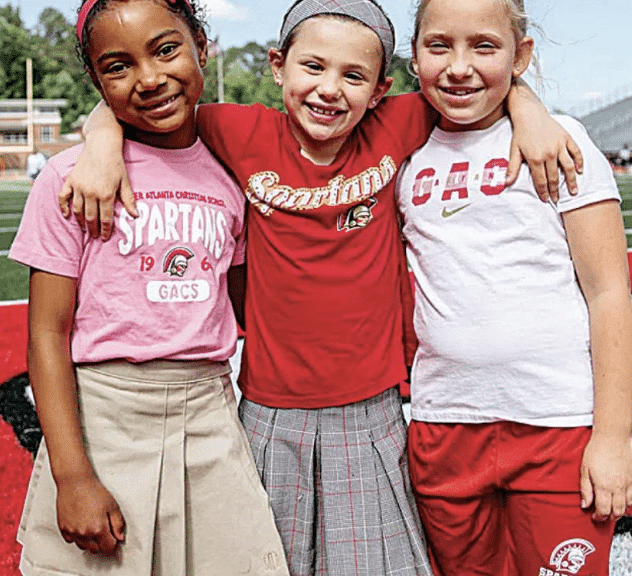 Three young girls wearing red, white and pink smiling for the camera at GAC summer camp