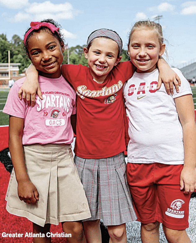 Three young girls wearing red, white and pink smiling for the camera at GAC summer camp