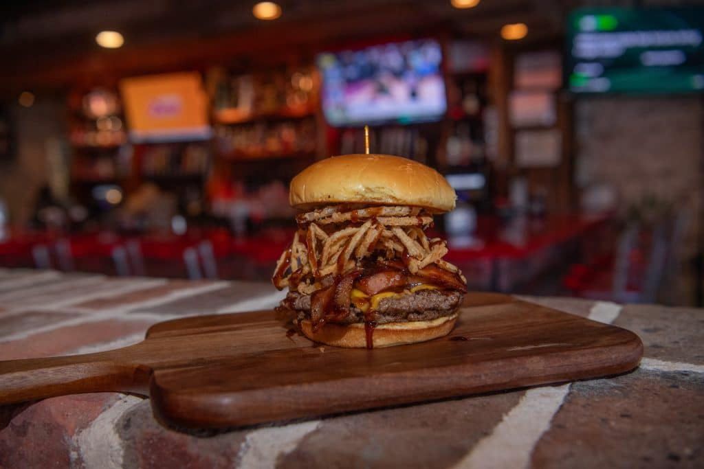 a large burger on a wooden board on a restaurant table