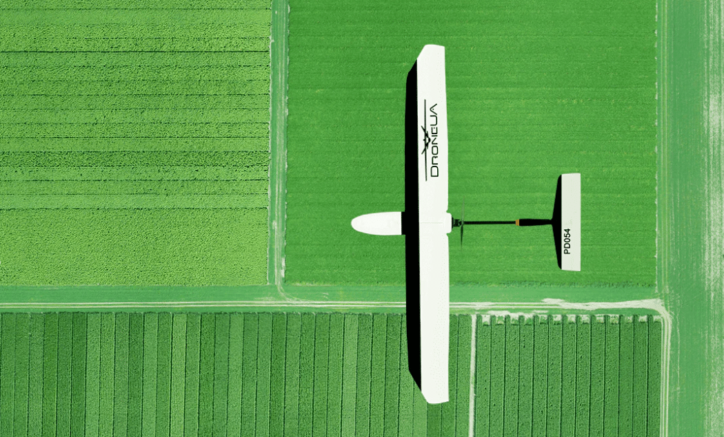 Overhead view of a white drone above a green farmland field.