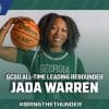 Black female college basketball player, Jada Warren, wearing a green jersey, holding a basketball on her shoulder and smiling at the camera.